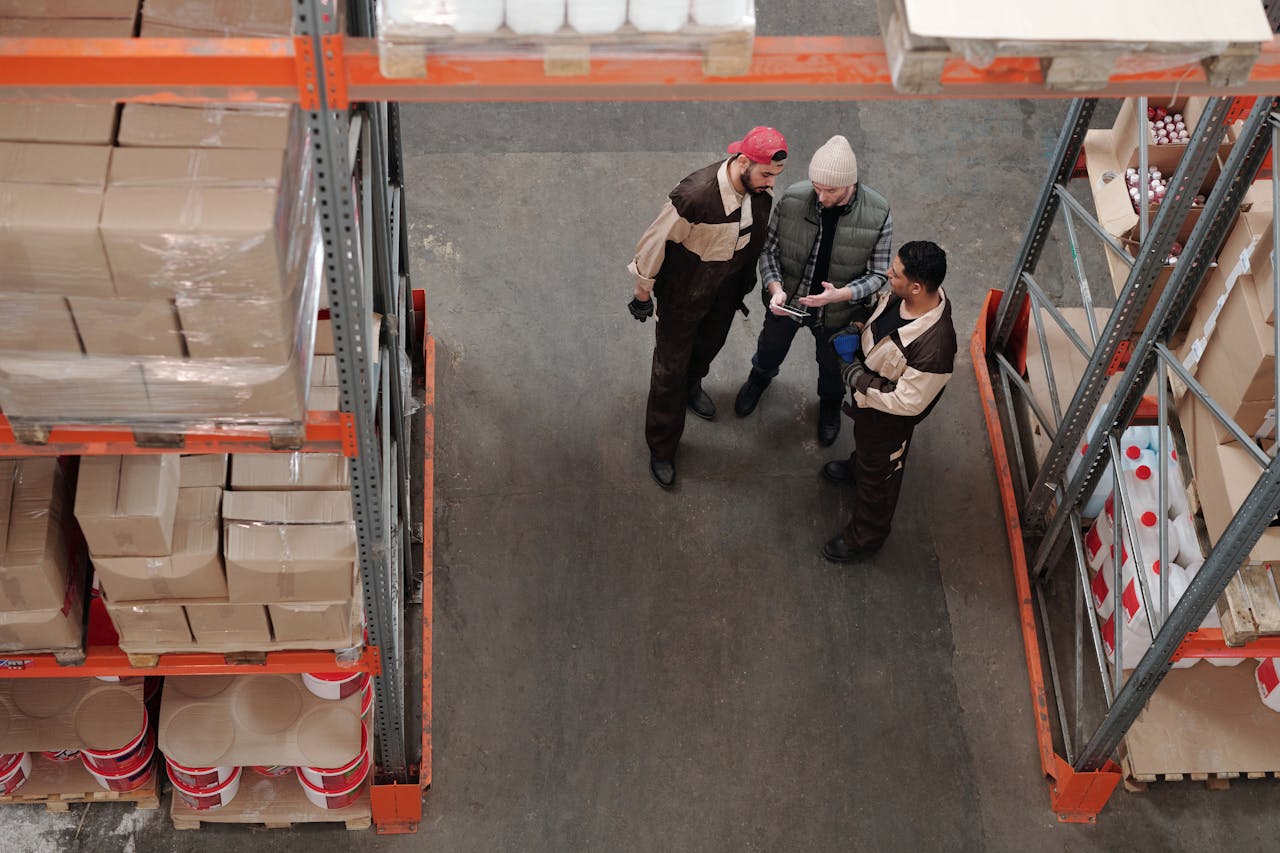 Three warehouse workers discussing logistics in an industrial storage area.